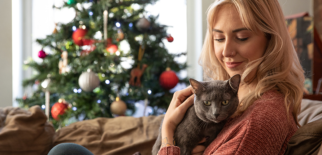 a woman holding a cat sitting on a couch in front of a christmas tree